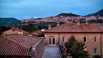 A courtyard with a brick building, a pathway, and a view of a historic town with a hill in the background.