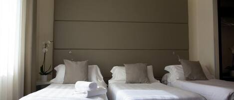 A hotel room with two beds, a large wall-mounted headboard, and a potted plant.