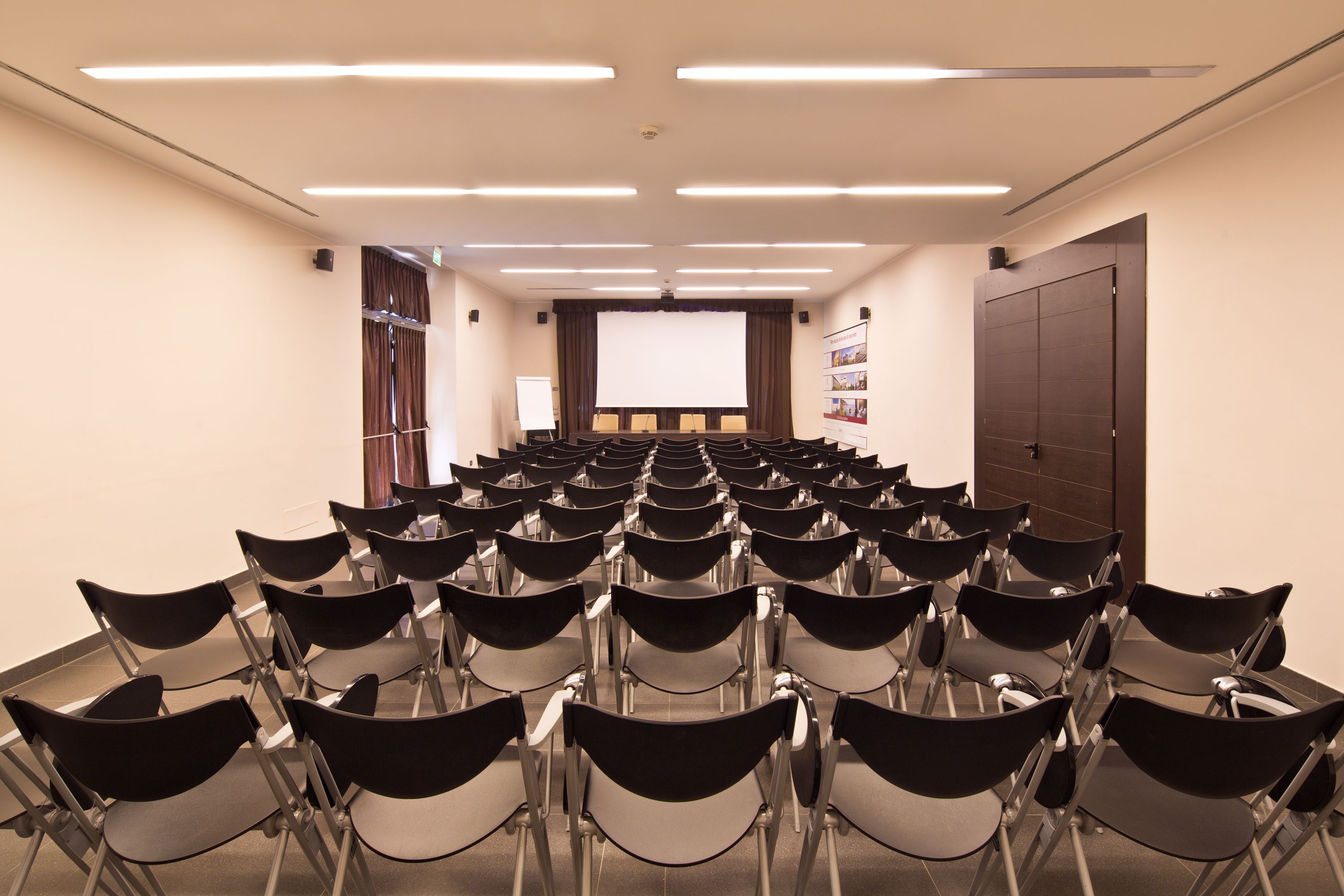A conference room with rows of chairs, a projector screen, and a whiteboard.