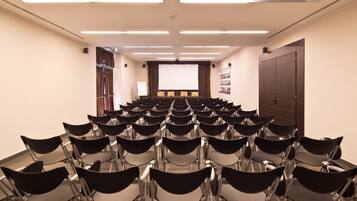 Una sala conferenze con file di sedie, uno schermo per proiettore e una lavagna.