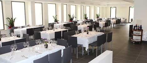 A spacious dining area with multiple tables set for a formal meal, featuring white tablecloths and black chairs.