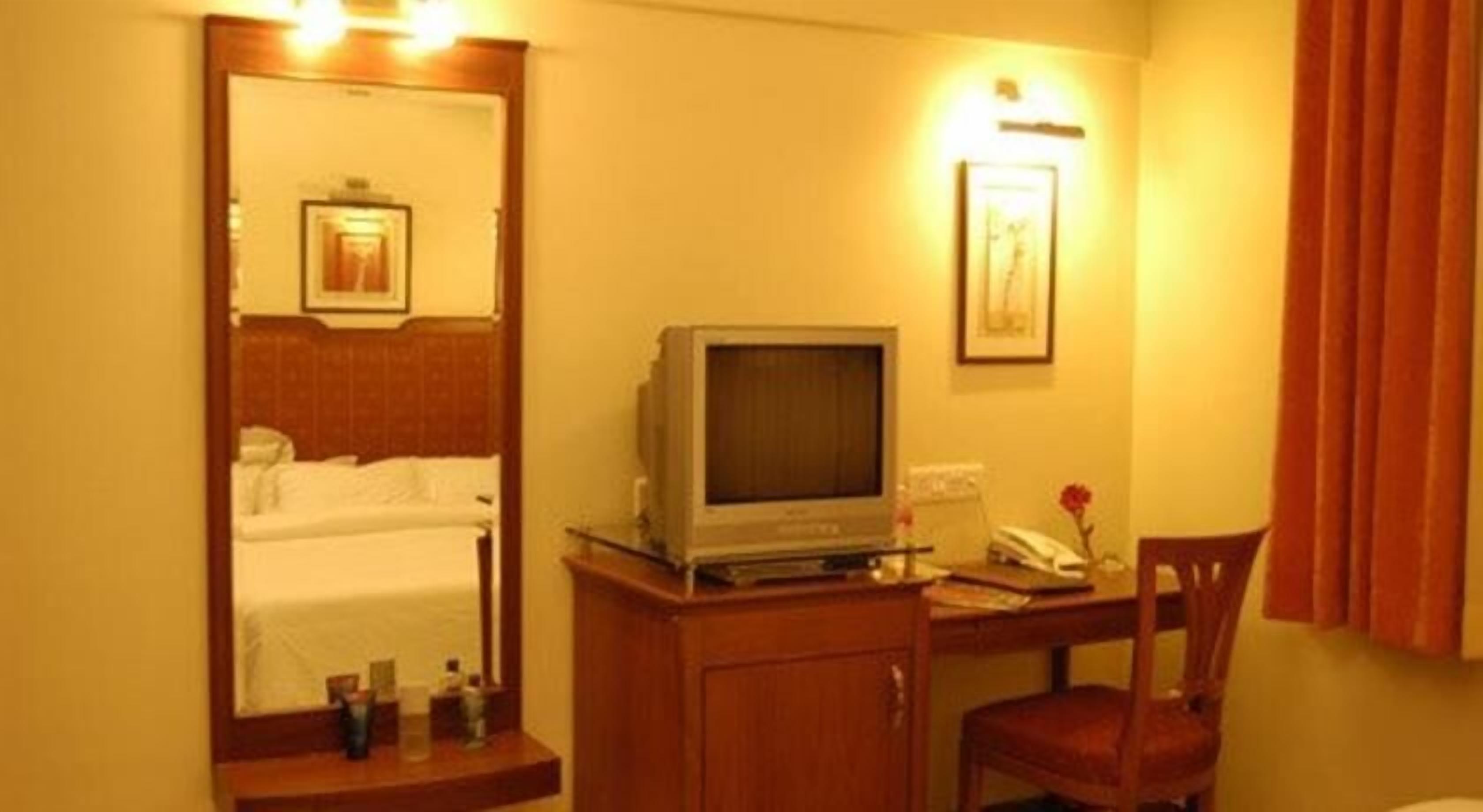 A hotel room with a bed, a desk with a television, a chair, and a mirror.