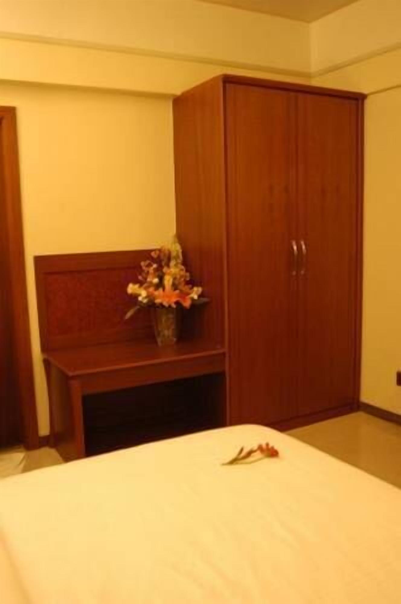A bedroom with a bed, a wooden wardrobe, and a small table with a vase of flowers.