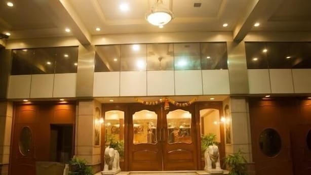 A hotel entrance with a grand wooden double door, steps leading up to it, and a seating area with chairs and potted plants. - Hotel Solitaire (Mumbai)