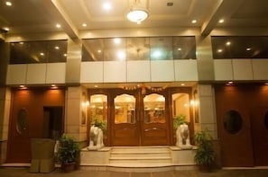 Entrada de hotel con una imponente puerta doble de madera, escalones que conducen a ella y un área de descanso con sillas y plantas en macetas.