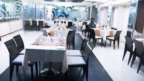 A modern restaurant with round tables and black chairs, featuring a glass wall with abstract designs. - Hotel Solitaire (Mumbai)