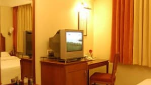 A hotel room with a bed, a desk with a television, a chair, and a mirror. - Hotel Solitaire (Mumbai)