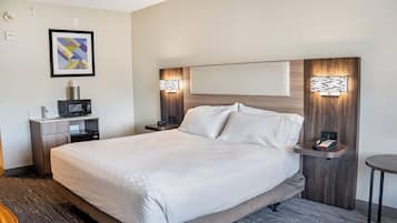 A hotel room with a large bed, a bedside table with a phone, a small desk with a microwave, and a framed picture on the wall.