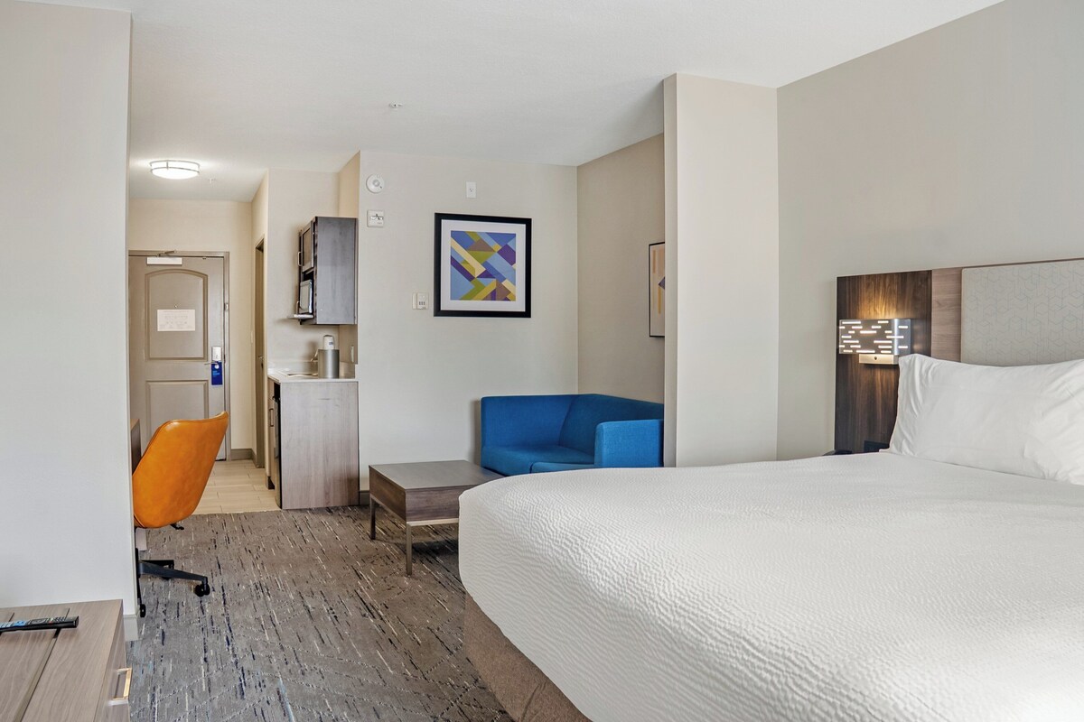 A hotel room with a large bed, a desk with a chair, a small table, and a blue sofa.