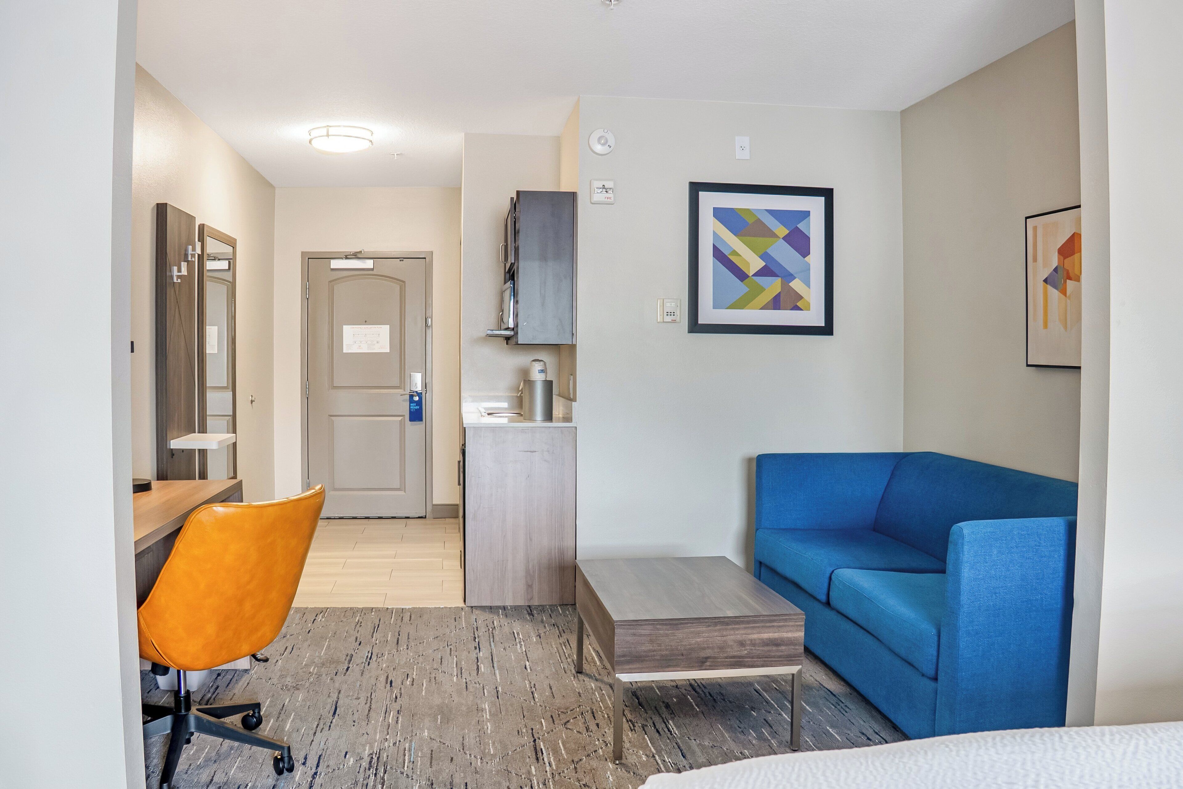 A hotel room with a desk, orange chair, blue sofa, and a small table.