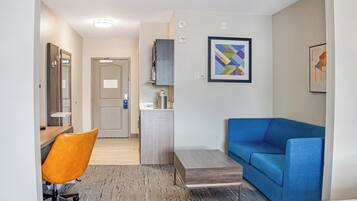 A hotel room with a desk, orange chair, blue sofa, and a small table.