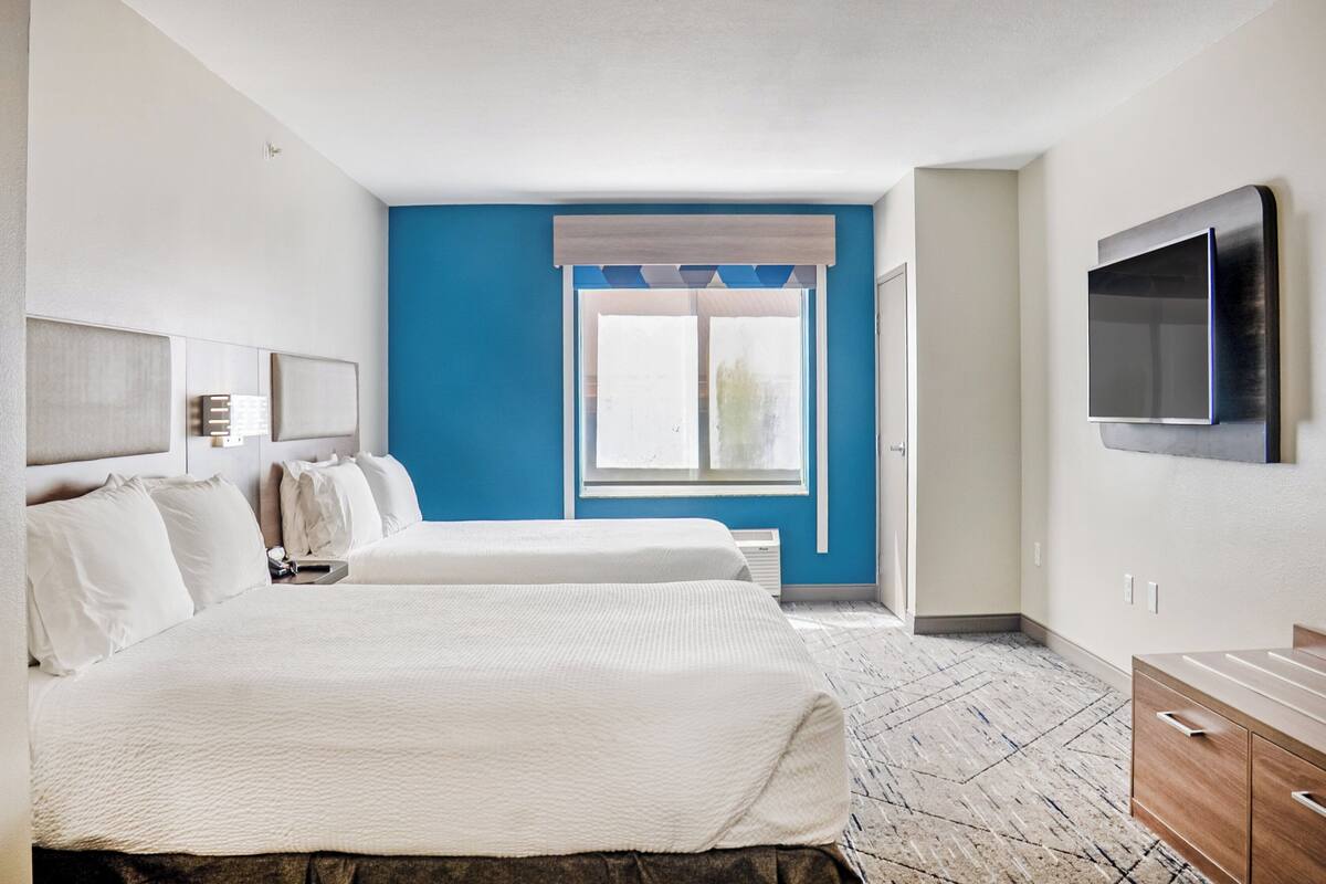 A hotel room with two beds, a large window with a view, a flat-screen TV mounted on the wall, and a wooden dresser.