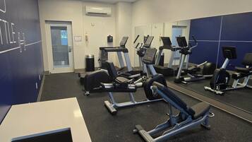 Un gimnasio con máquinas de cardio, un muro de espejos y una puerta que da a otra sala.