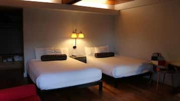 A room with two beds, a nightstand with a lamp, a red chair, and a wooden ceiling.