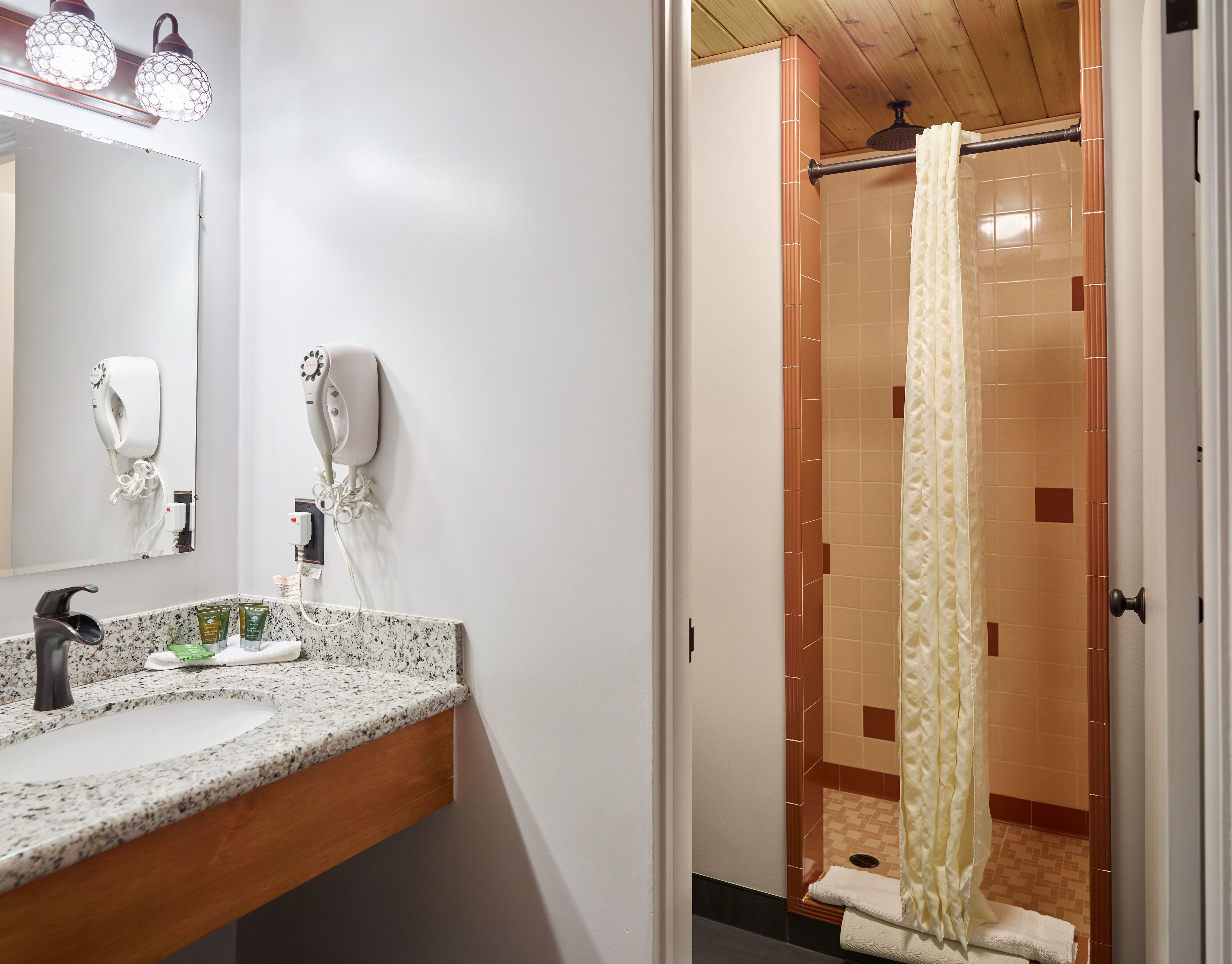 Un baño con encimera de granito, un espejo, dos secadores de pelo y una ducha con cortina color beige.