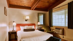 A hotel room with a large bed, two bedside lamps, a chair, a mirror, and a window with curtains.