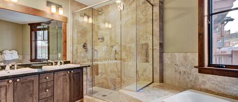 A modern bathroom with a glass-enclosed shower, a double sink vanity, and a large bathtub.