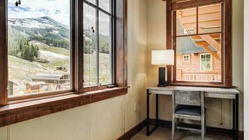 A room with a large window offering a view of a mountainous landscape, a desk with a chair, and a lamp.