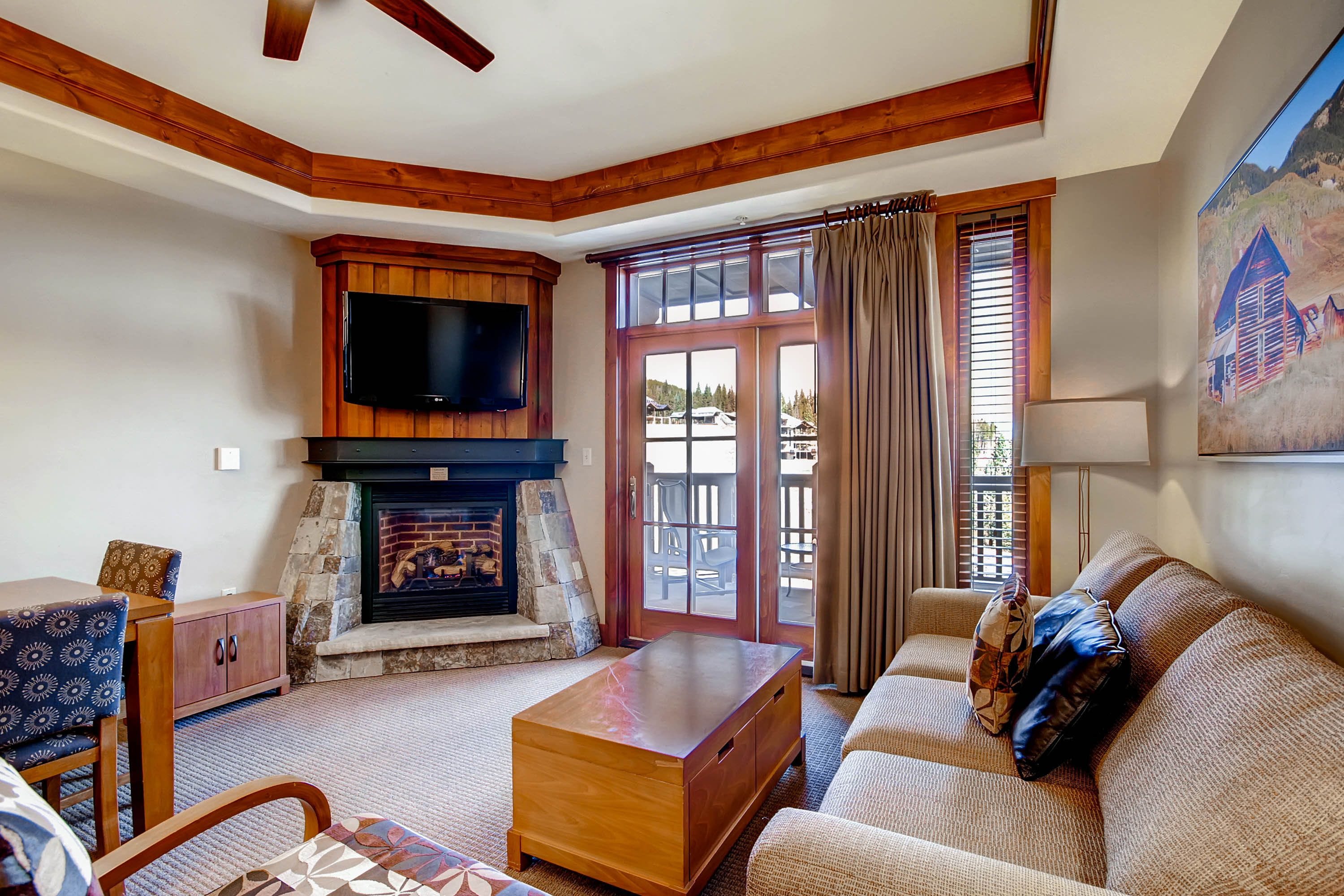 A cozy living room with a stone fireplace, a flat-screen TV, and a large window with curtains.