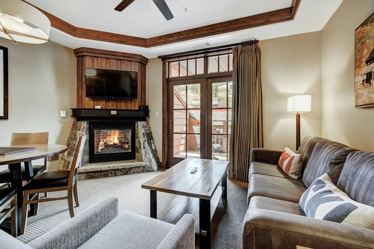 A cozy living room with a fireplace, a television mounted above it, a sofa, a coffee table, and a dining area with a table and chairs.