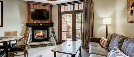 A cozy living room with a fireplace, a television mounted above it, a sofa, a coffee table, and a dining area with a table and chairs.