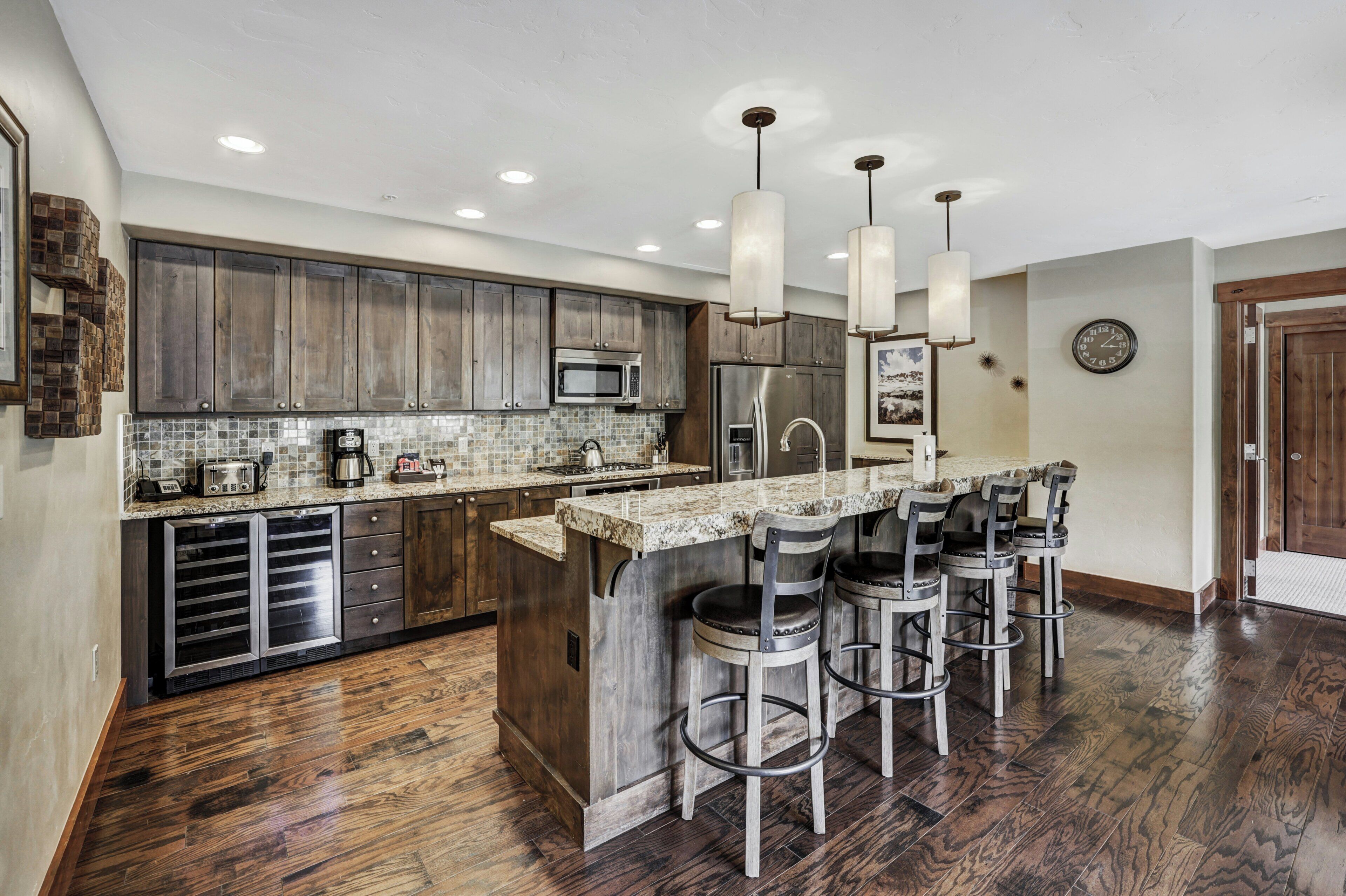 A modern kitchen with dark wood cabinets, stainless steel appliances, a granite countertop, and bar stools.