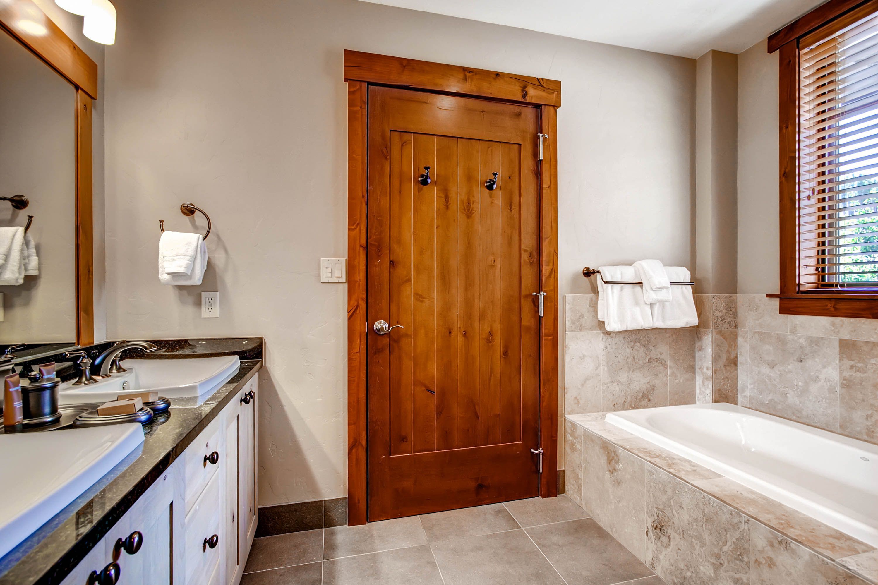 A bathroom with a wooden door, a bathtub, and a vanity with a sink and mirror.