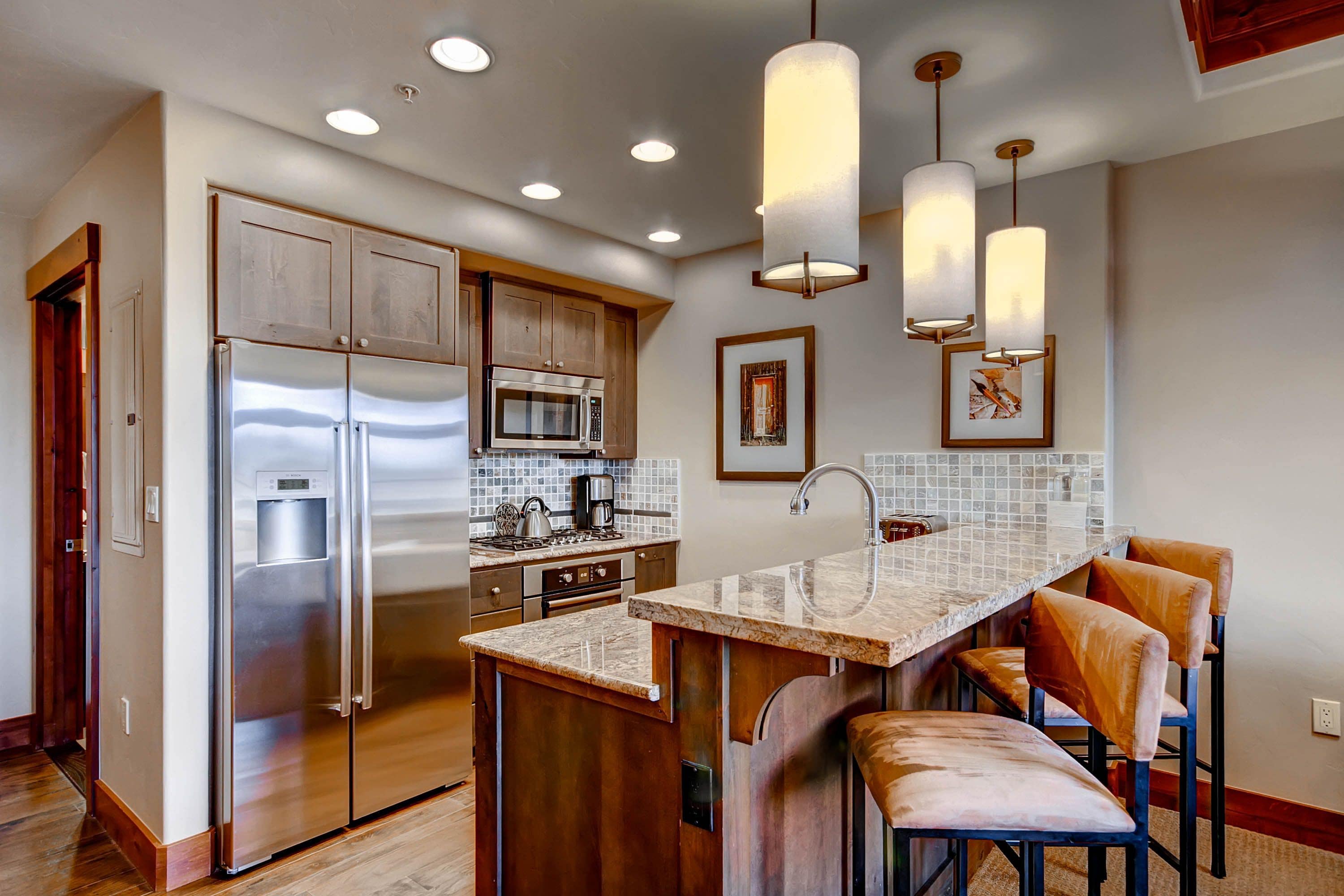 A modern kitchen with stainless steel appliances, wooden cabinets, and a marble countertop.