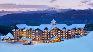 Un gran edificio de varios pisos con múltiples balcones y un techo cubierto de nieve, rodeado de montañas.