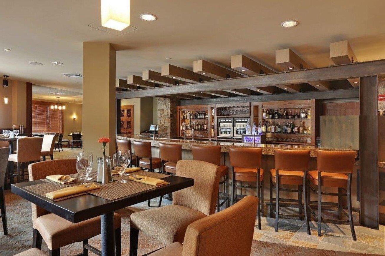 Um restaurante com área de bar, vigas de madeira no teto e banquetas.