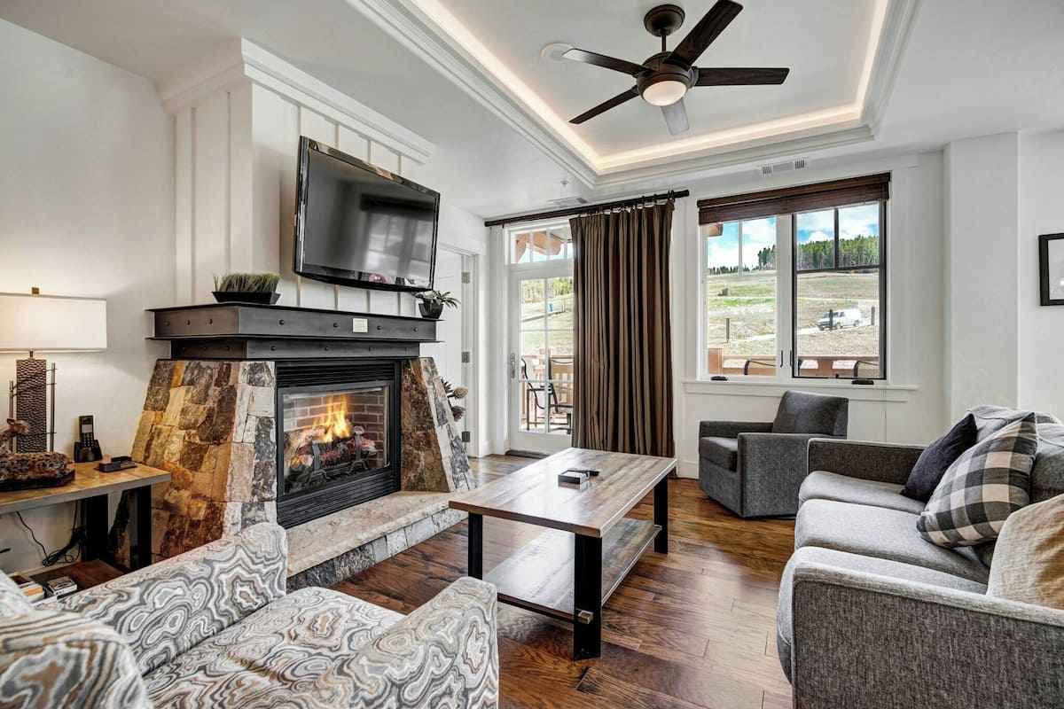 A living room with a fireplace, a flat-screen TV, and a ceiling fan.
