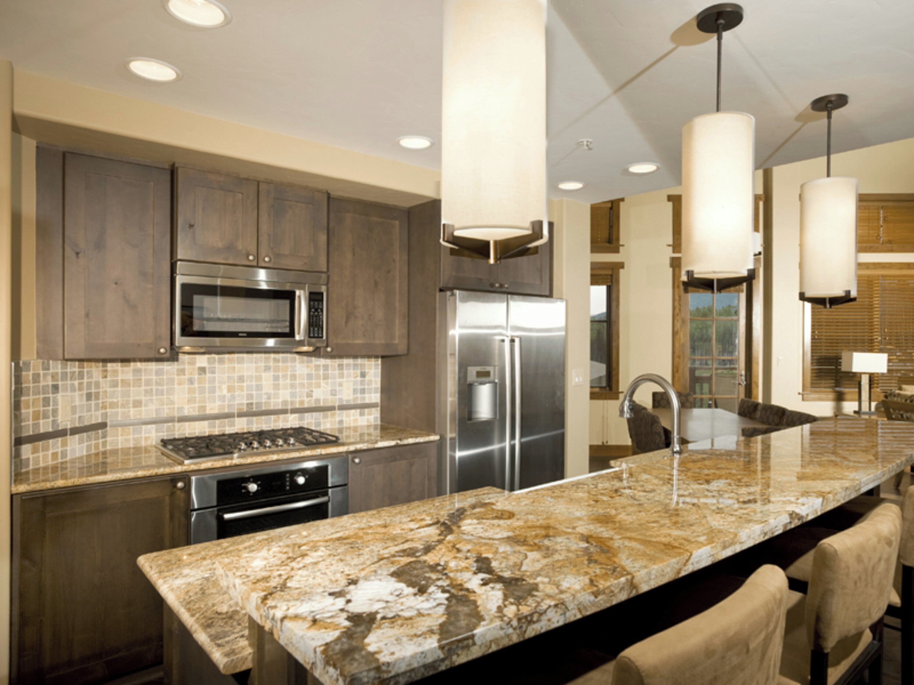 A modern kitchen with granite countertops, stainless steel appliances, and pendant lighting.