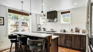 Una cocina moderna con una isla central, taburetes de bar, armarios de madera y ventanas amplias.