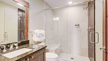 A modern bathroom with a glass-enclosed shower, a double sink vanity, and a toilet.