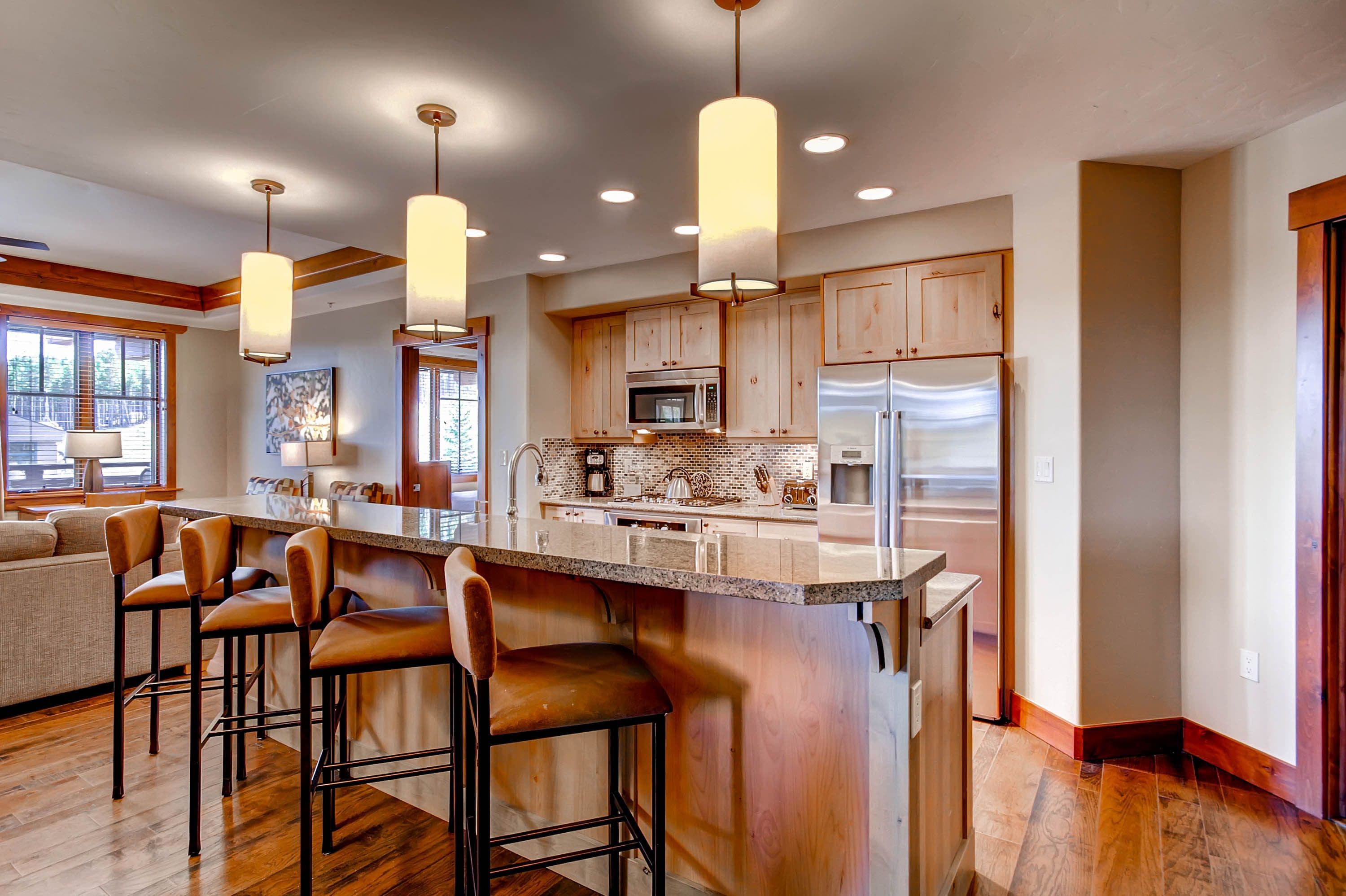 A modern kitchen with a central island, bar stools, wooden cabinets, and pendant lighting.