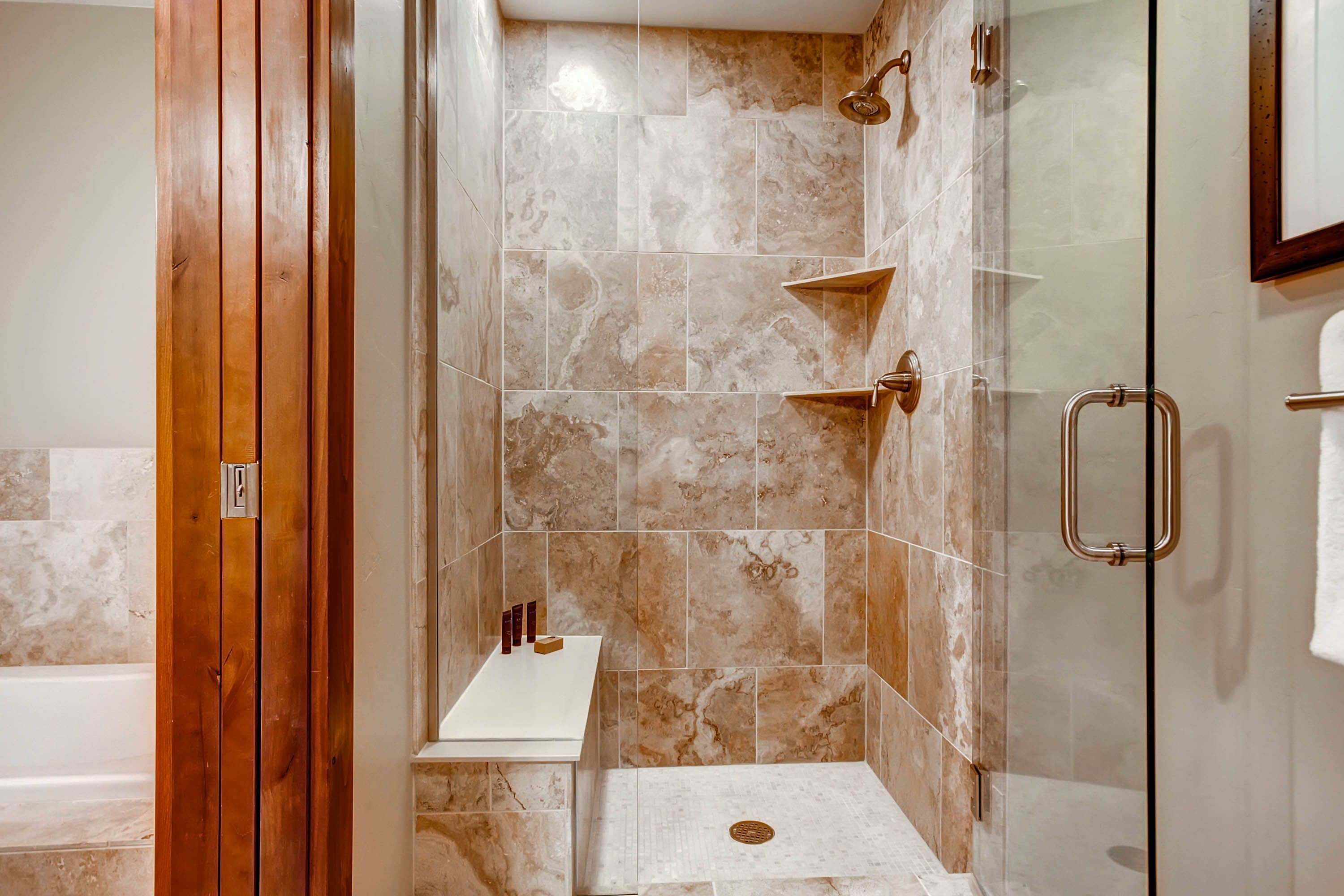 A modern bathroom with a glass-enclosed shower, marble tiles, and a wooden door.