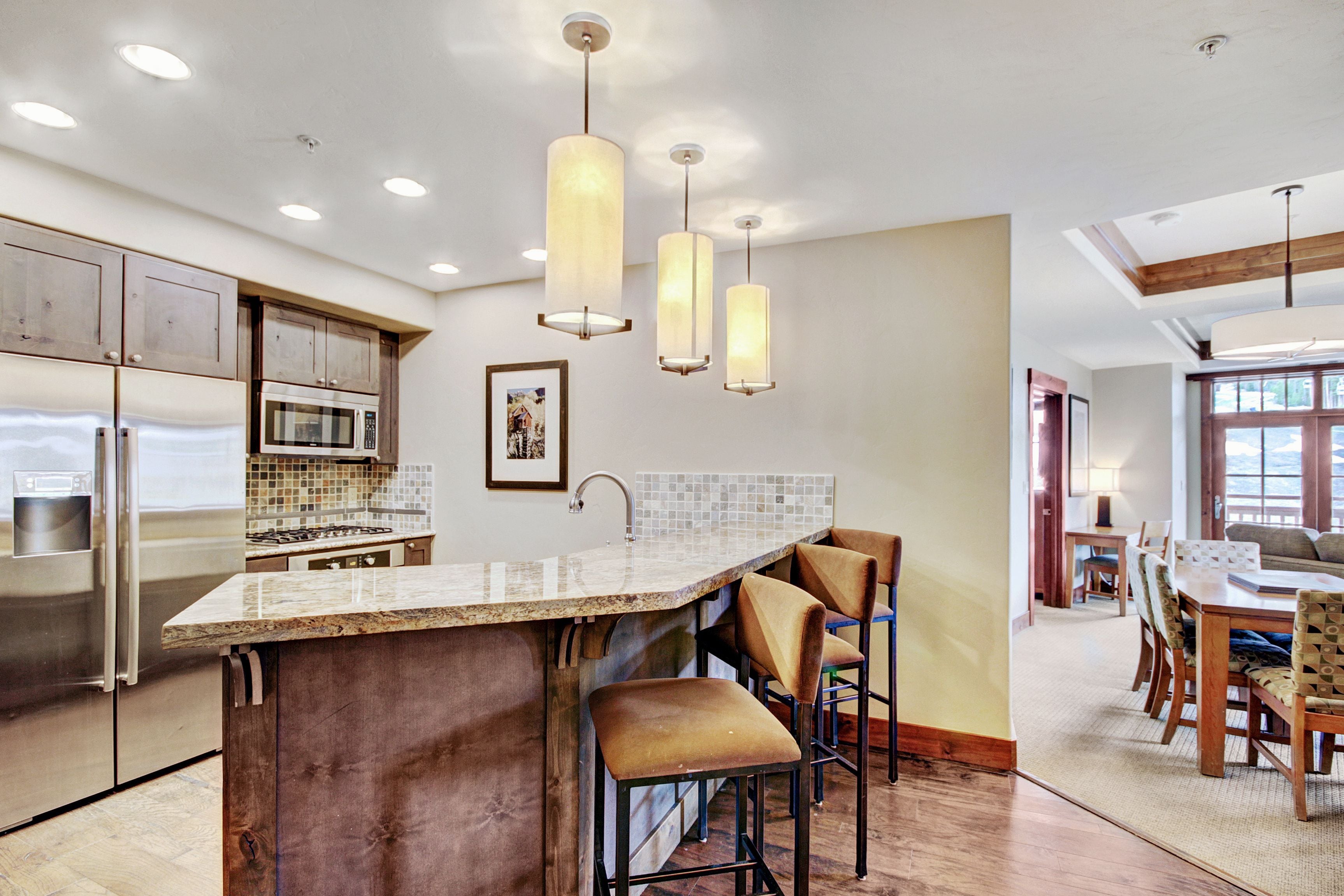 A modern kitchen with a central island, bar stools, and a dining area with a wooden table and chairs.