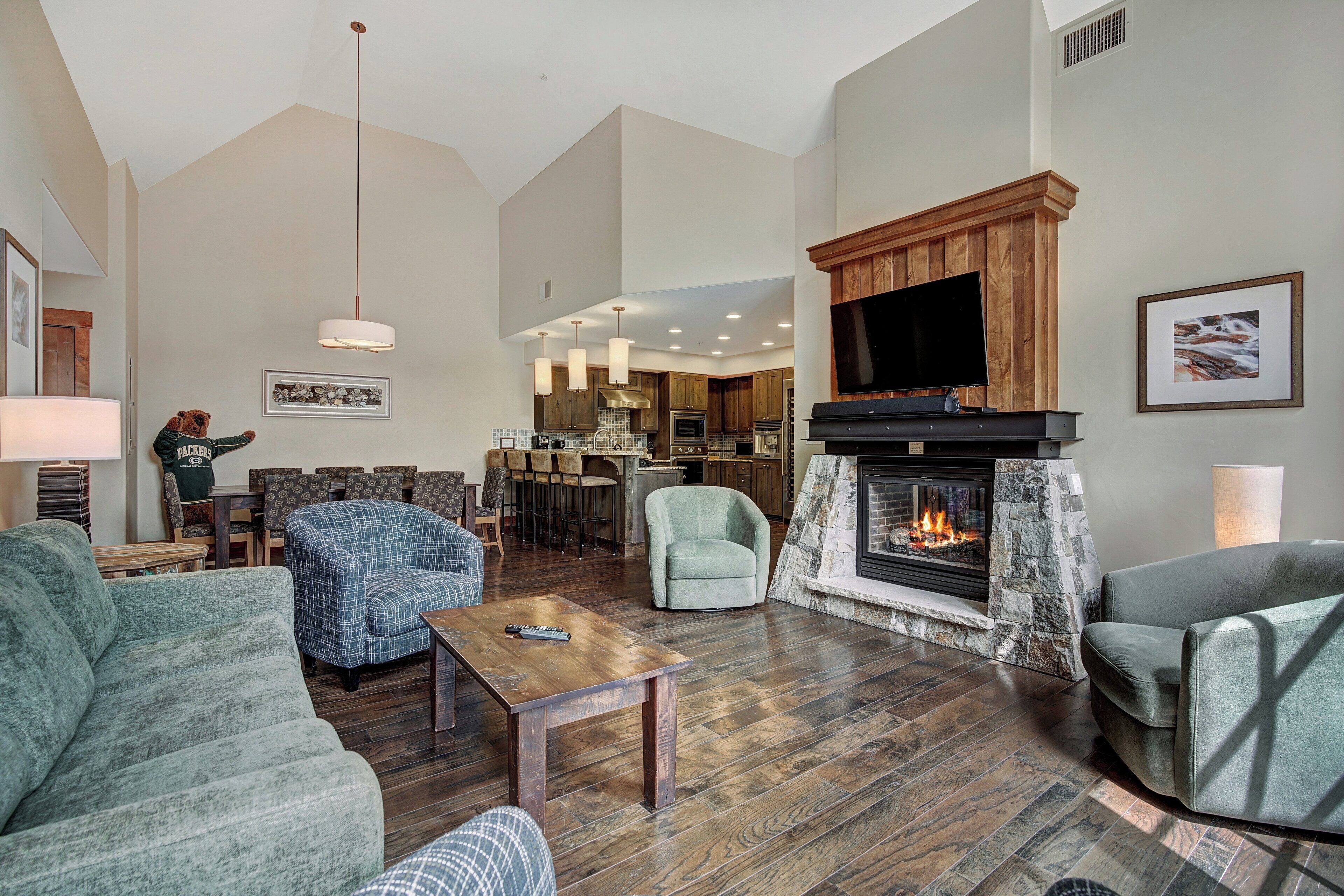 A spacious living room with a fireplace, comfortable seating, and a kitchen area in the background.