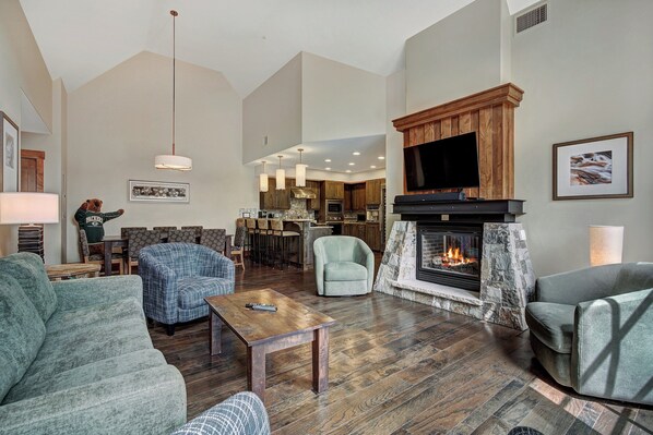A spacious living room with a fireplace, comfortable seating, and a kitchen area in the background.