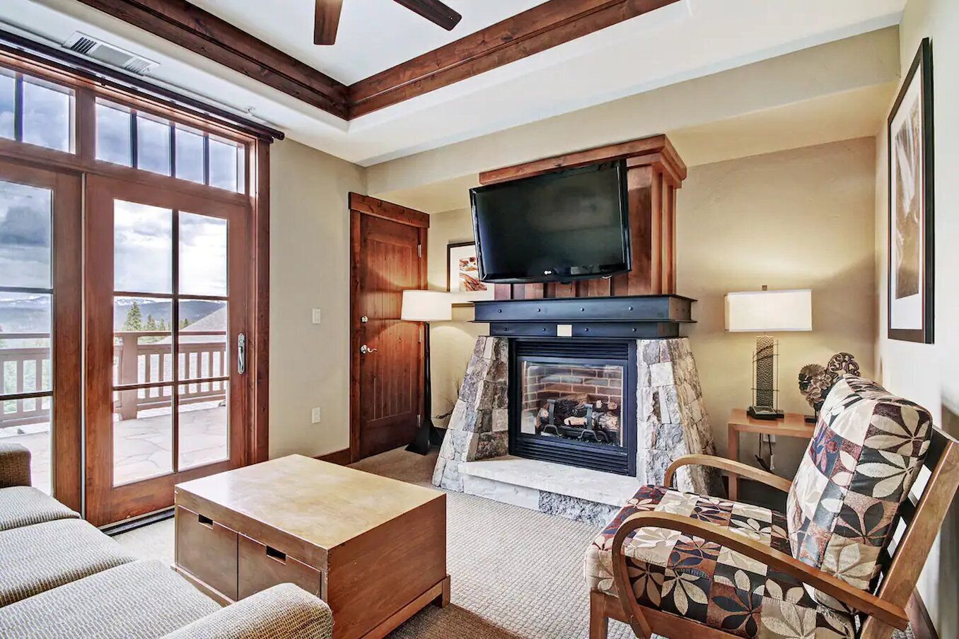 A cozy living room with a fireplace, a television mounted above it, and a large window offering a view of the outdoors.