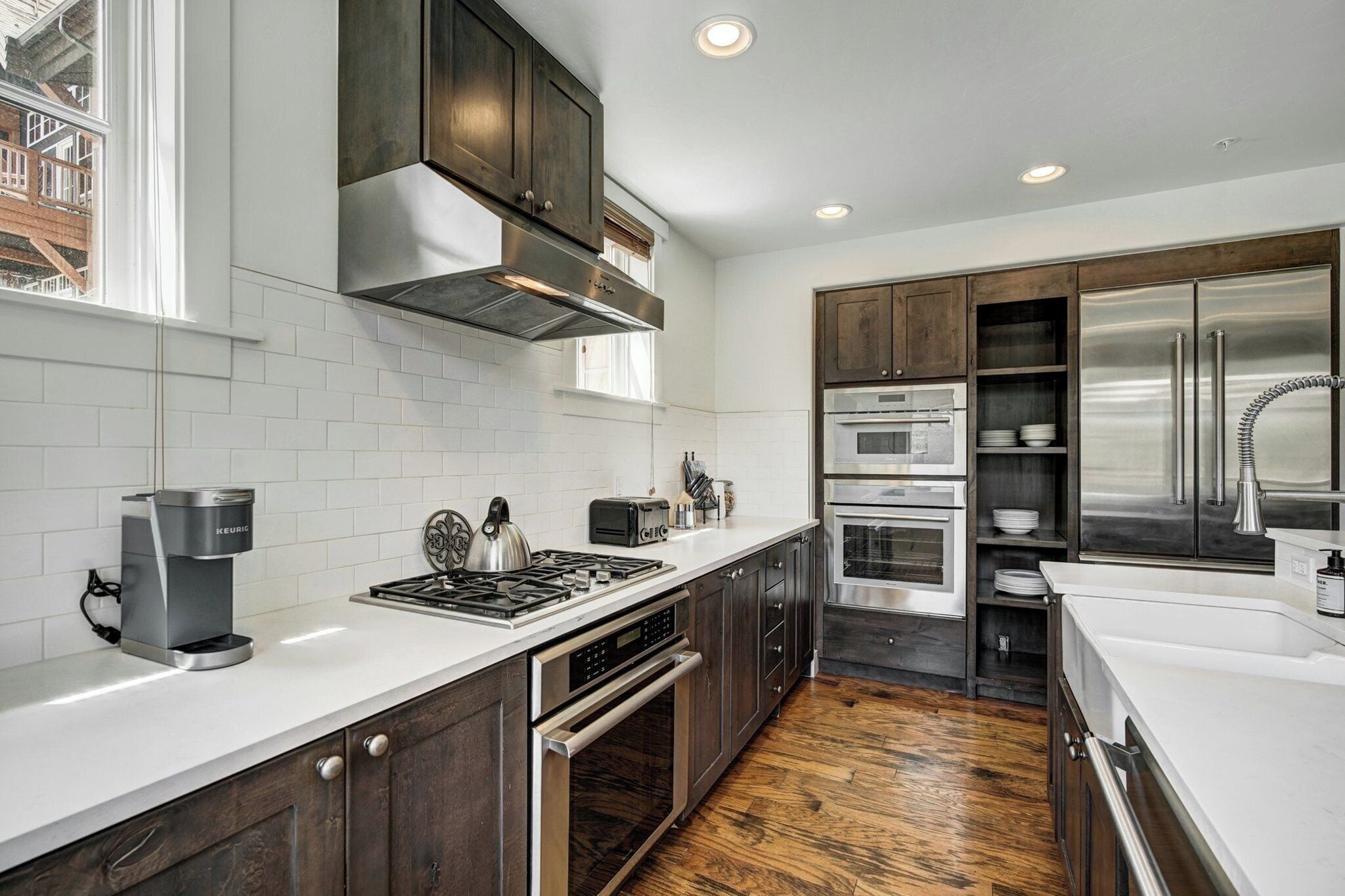 A modern kitchen with dark wood cabinets, white countertops, stainless steel appliances, and a view of the city through large windows.