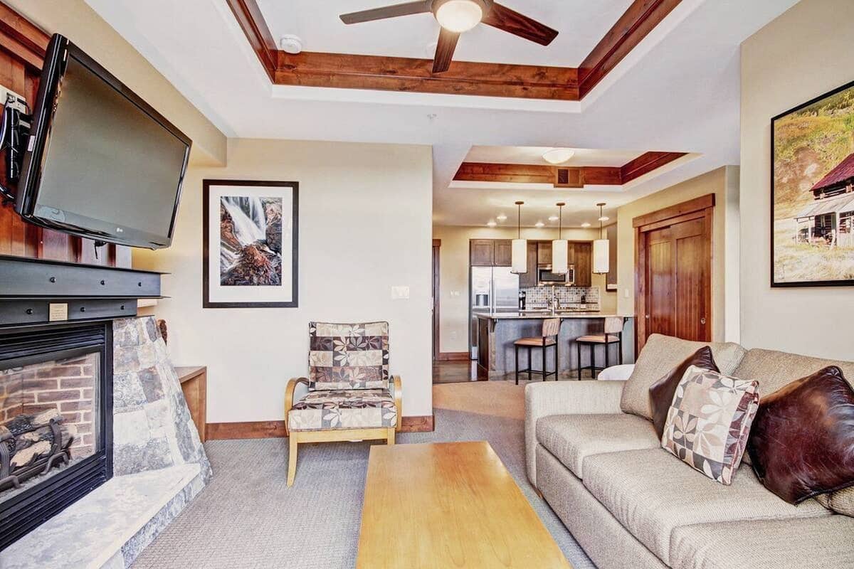 A living room with a fireplace, a television, a dining area, and a kitchen in the background.