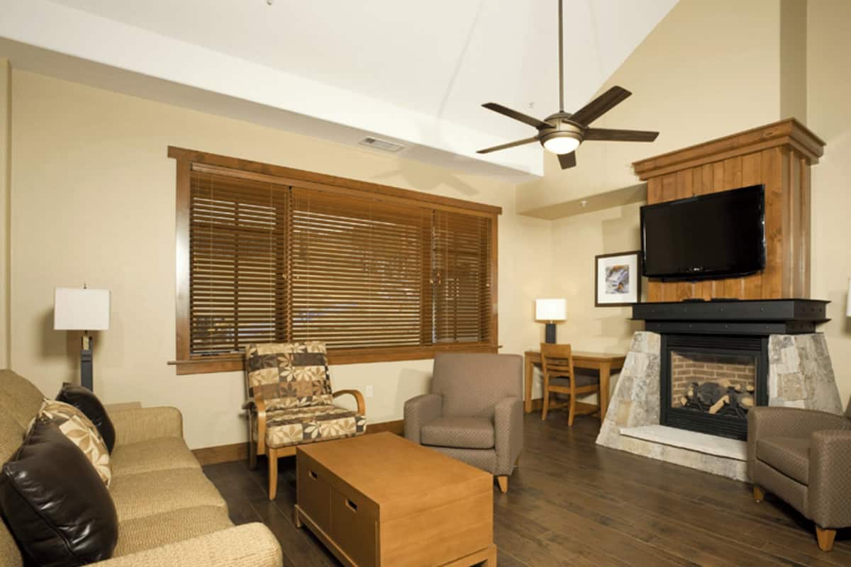 A living room with a fireplace, wooden flooring, and a ceiling fan.