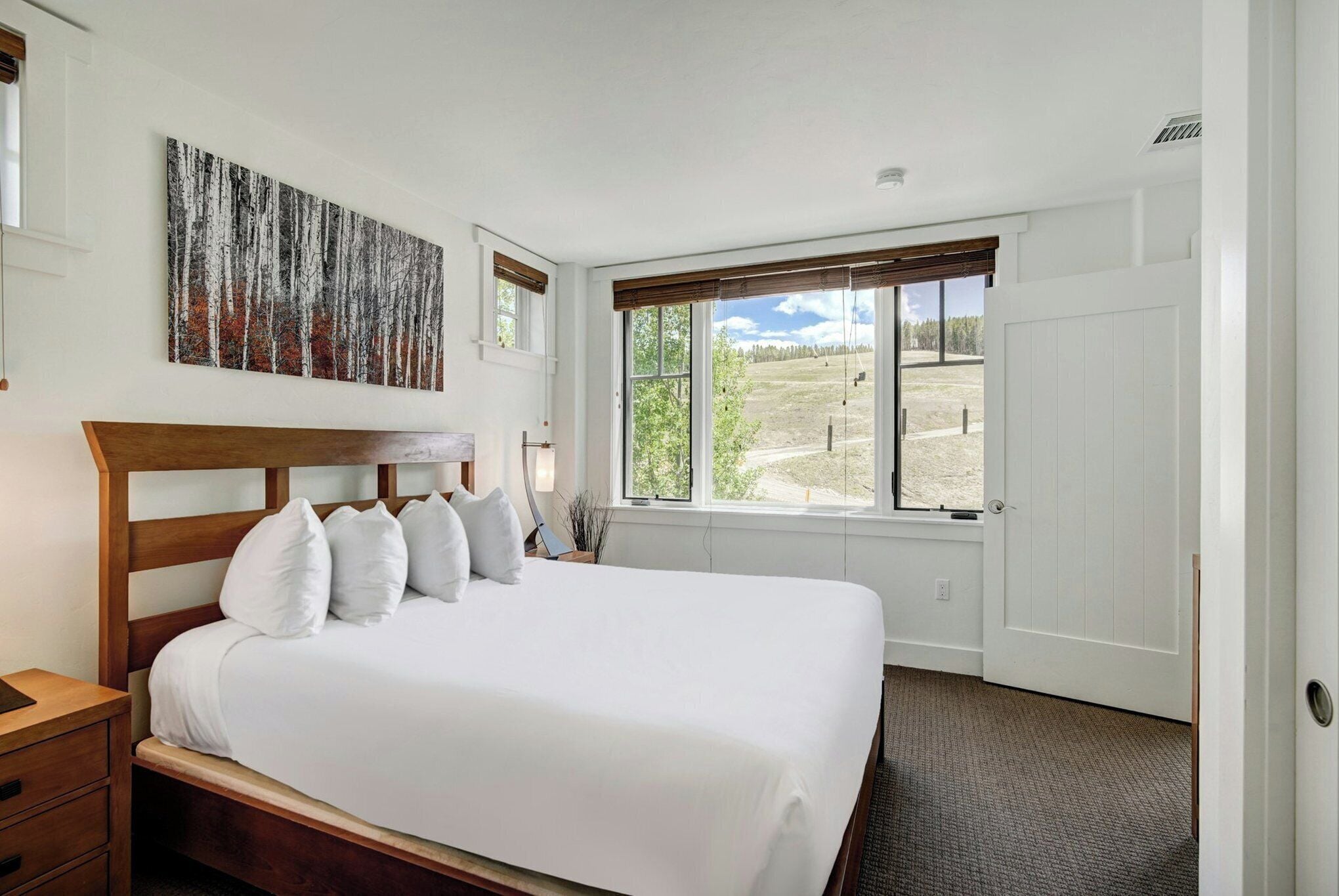 A bedroom with a large bed, a window with a view of a field, and a painting on the wall.
