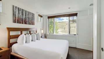 A bedroom with a large bed, a window with a view of a field, and a painting on the wall.