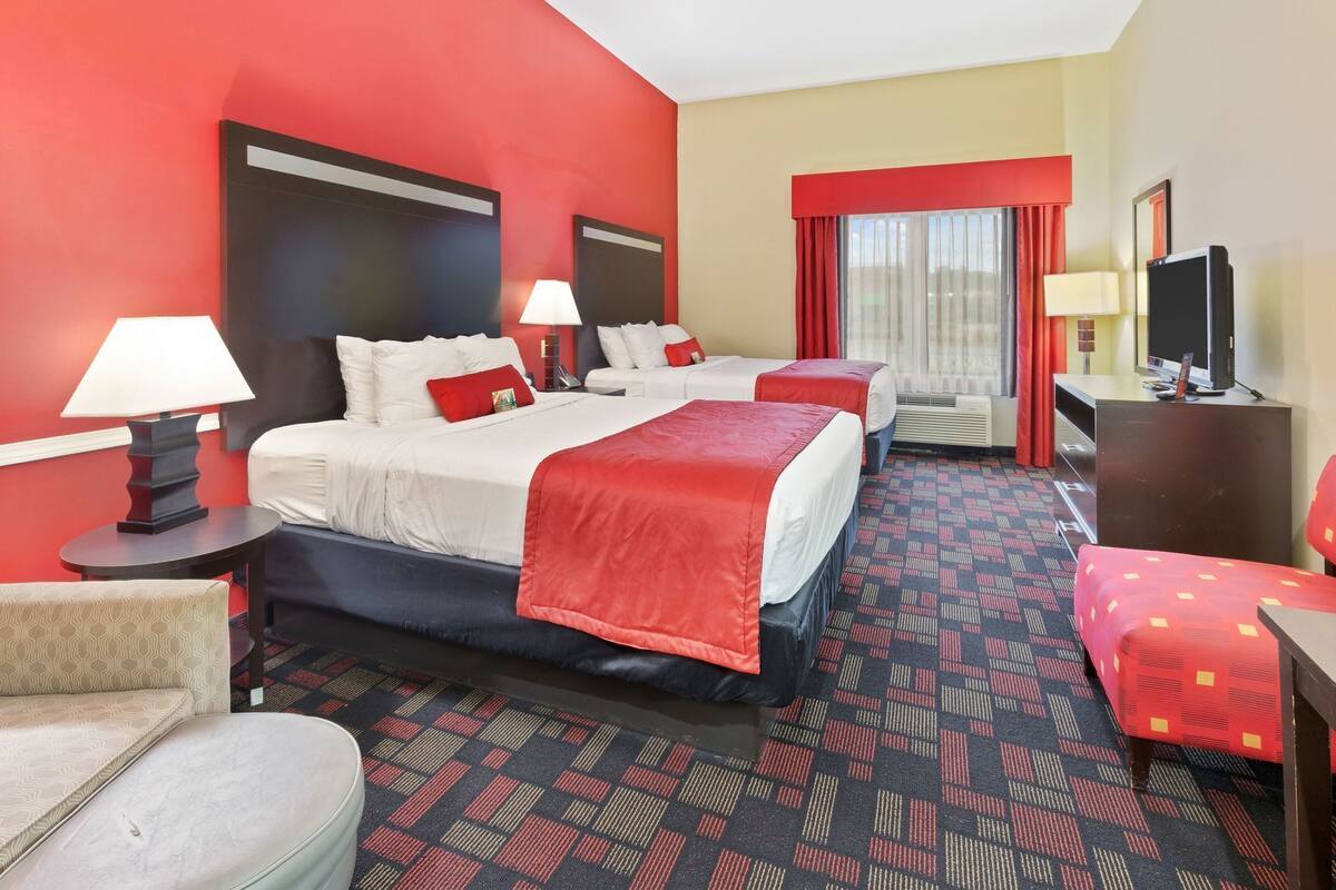 Ein Hotelzimmer mit zwei Betten, einem Schreibtisch, einem Sessel und einem Fernseher.