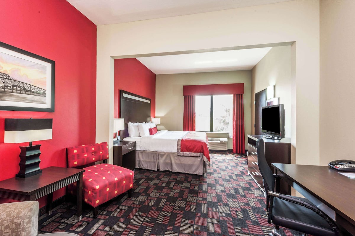 Ein Hotelzimmer mit Bett, Schreibtisch, Stuhl, Fernseher und einem Fenster mit Vorhängen.