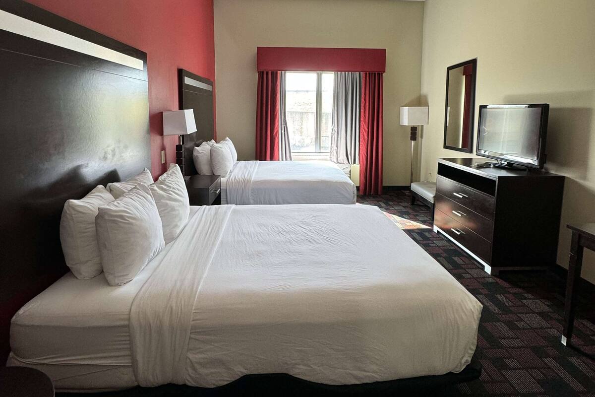Ein Hotelzimmer mit zwei Betten, einem Fernseher, einem Schreibtisch und einem Fenster mit Vorhängen.