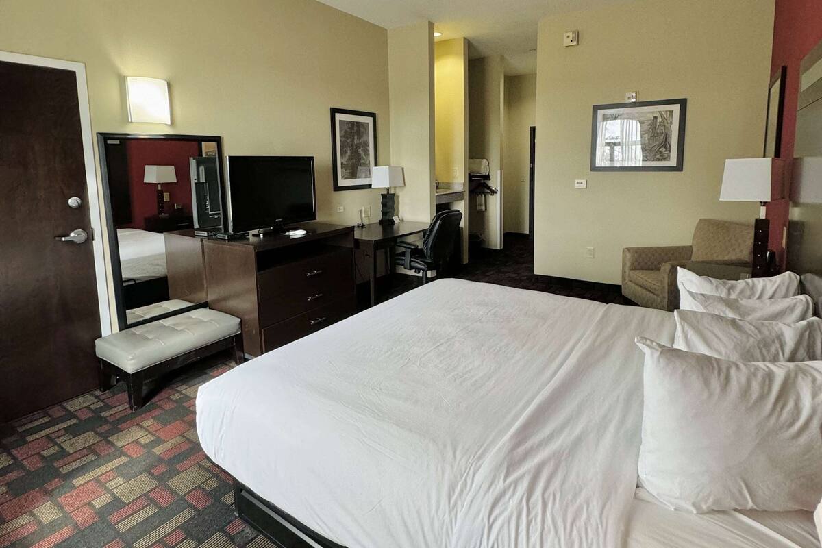 Ein Hotelzimmer mit einem großen Bett, einem Schreibtisch mit Stuhl, einem Fernseher und einem Spiegel.