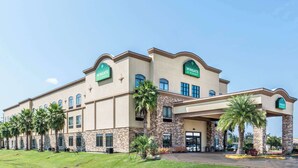 A Wingate hotel with a large building, palm trees, and a clear sky. - Wingate by Wyndham Lake Charles Casino Area (Lake Charles)